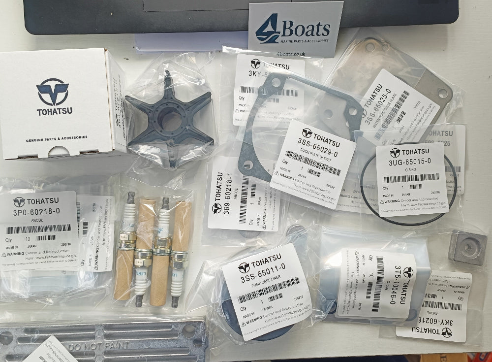 Assorted boat parts including impellers and gaskets on a table with a laptop in the background.