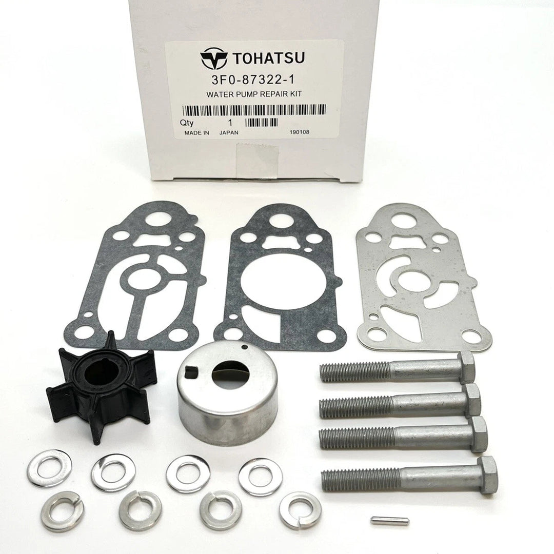 Tohatsu water pump repair kit parts arranged on a white surface, including metal gaskets, bolts, washers, a black impeller, a metal housing, and the original white product box with Tohatsu branding.